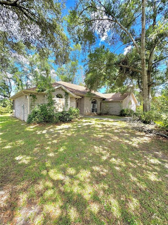 A single-story brick house with a gabled roof sits on a grassy, tree-shaded lot — 571 NW ZACK DRIVE, LAKE CITY, FL