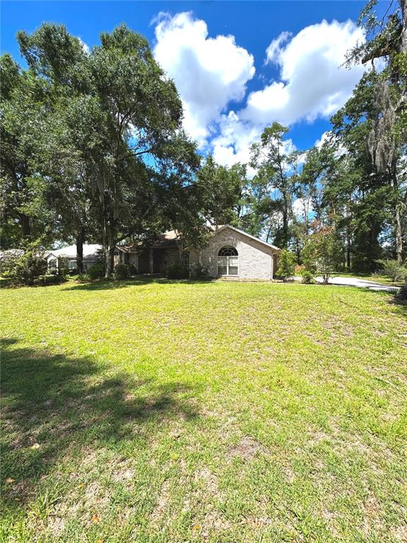 A single-story brick house sits behind a large grassy lawn under a blue sky — 571 NW ZACK DRIVE, LAKE CITY, FL