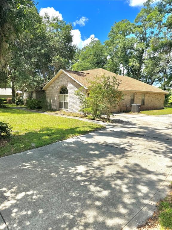 A single-story brick house with a concrete driveway and mature trees in the yard — 571 NW ZACK DRIVE, LAKE CITY, FL