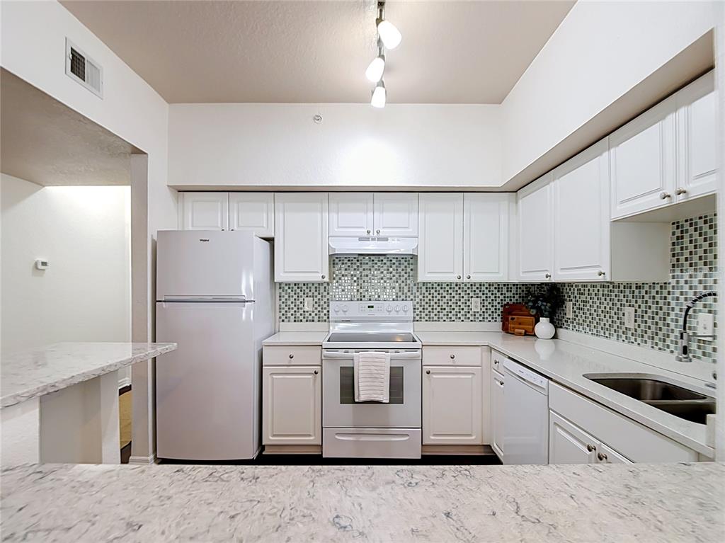 A kitchen features white cabinets, a mosaic tile backsplash, a dishwasher, and a breakfast bar — 501 S MOODY AVENUE UNIT 1139B, TAMPA, FL