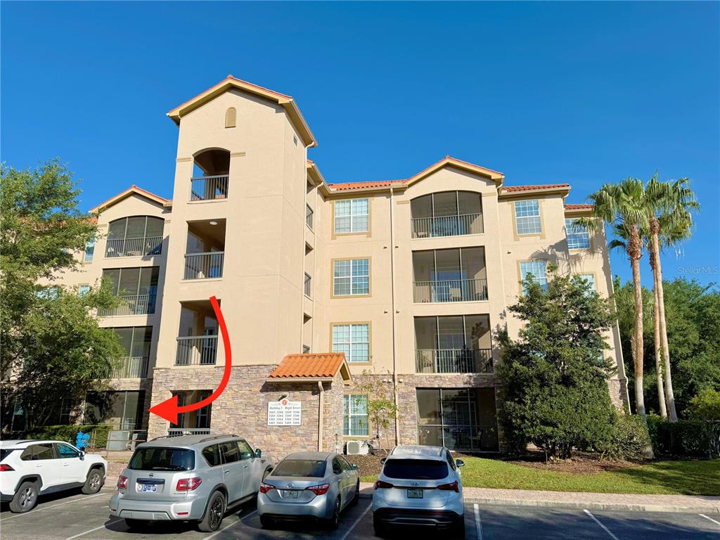 A multi-story apartment building exterior with a red arrow pointing toward a ground-floor patio — 8010 TUSCANY WAY UNIT 3103, DAVENPORT, FL
