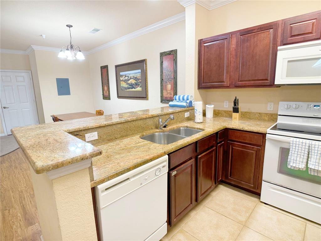 A kitchen features dark wood cabinets, granite countertops, a white dishwasher, and a white stove — 8010 TUSCANY WAY UNIT 3103, DAVENPORT, FL