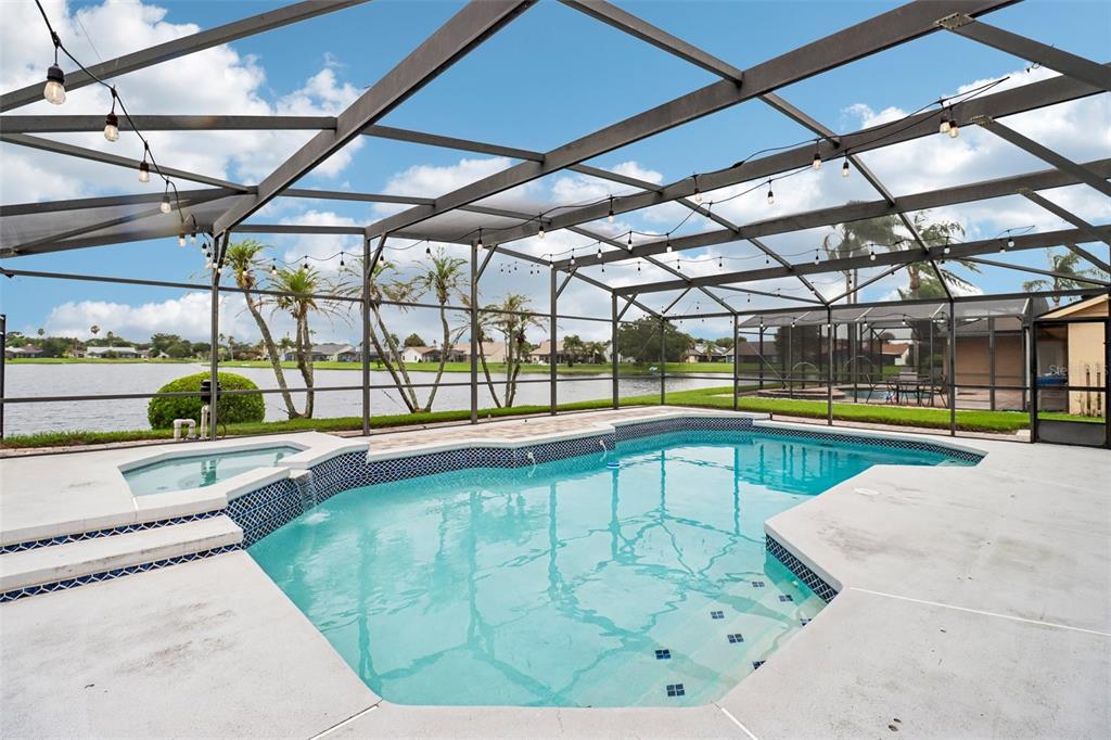 A screened-in swimming pool and spa overlook a lake under a clear blue sky — 14636 EAGLES CROSSING DRIVE, ORLANDO, FL