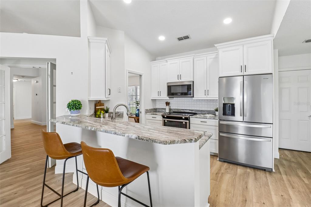 A kitchen features white cabinets, stainless steel appliances, a stone countertop, and two bar stools — 14636 EAGLES CROSSING DRIVE, ORLANDO, FL