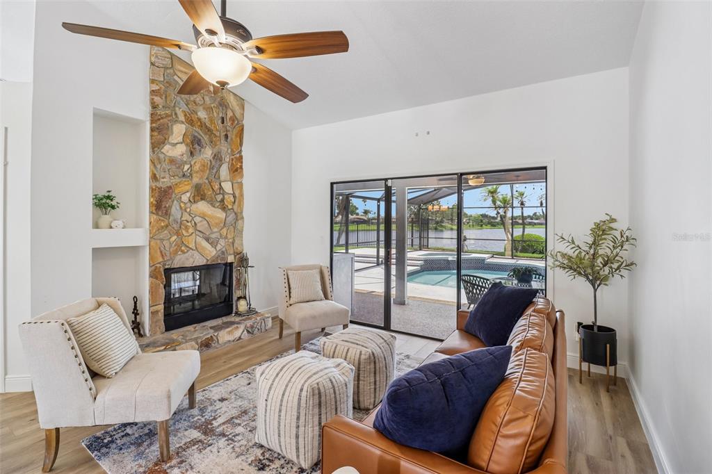 A living room features a stone fireplace, wood-look flooring, and sliding doors overlooking a pool — 14636 EAGLES CROSSING DRIVE, ORLANDO, FL