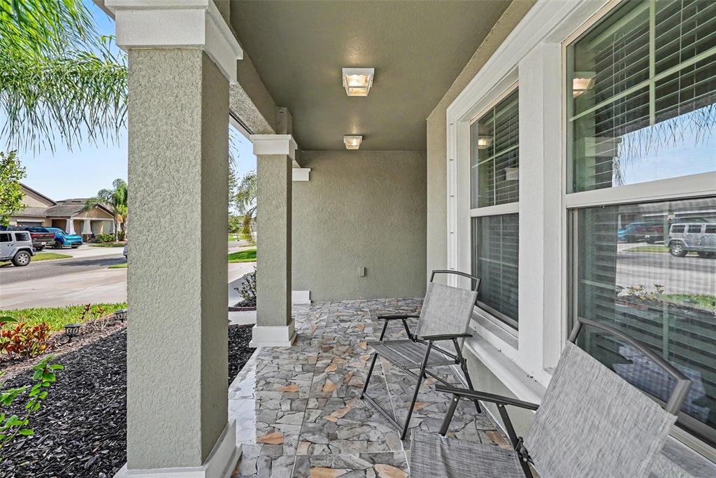 A covered front porch features stone-tiled flooring, two chairs, and two ceiling lights — 10829 CRUSHED GRAPE DRIVE, RIVERVIEW, FL