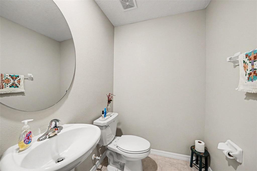 A half bathroom features a pedestal sink, a round mirror, and a white toilet — 10829 CRUSHED GRAPE DRIVE, RIVERVIEW, FL