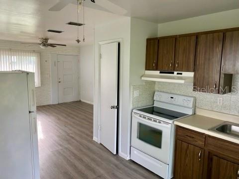 A kitchen with wood cabinets, a white stove, and a refrigerator opens into a living area — 4808 20TH STREET, ZEPHYRHILLS, FL