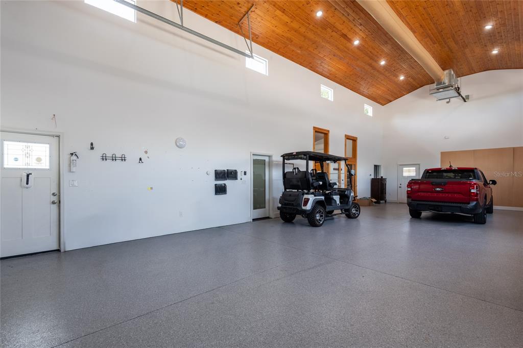 A spacious garage features a high wood-paneled ceiling, gray epoxy flooring, a golf cart, and a truck — 6757 AMANDA VISTA CIRCLE, LAND O LAKES, FL
