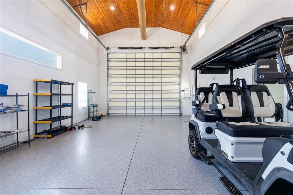 A spacious garage with a high wood-paneled ceiling, epoxy flooring, and a golf cart inside — 6757 AMANDA VISTA CIRCLE, LAND O LAKES, FL