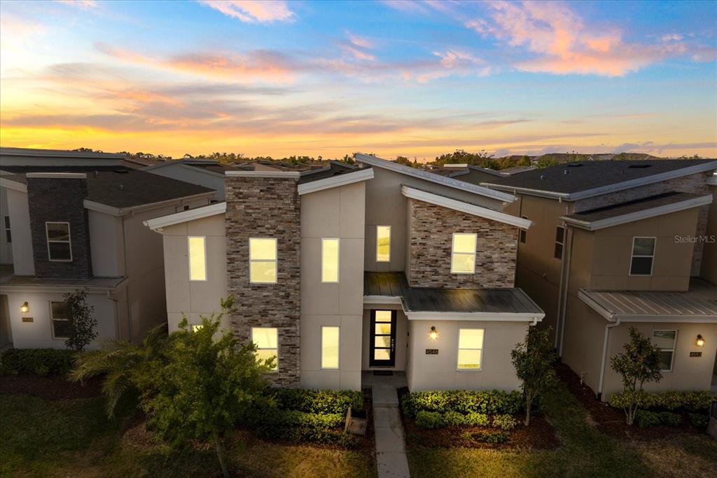 An exterior view of a modern two-story house with stone accents and a sunset sky — 4548 TARGET BOULEVARD, KISSIMMEE, FL