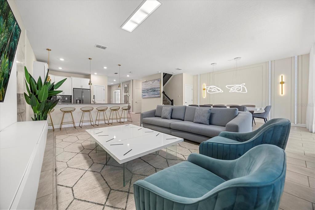 A modern open-concept living room features a grey sofa, blue armchairs, and a white coffee table — 4548 TARGET BOULEVARD, KISSIMMEE, FL