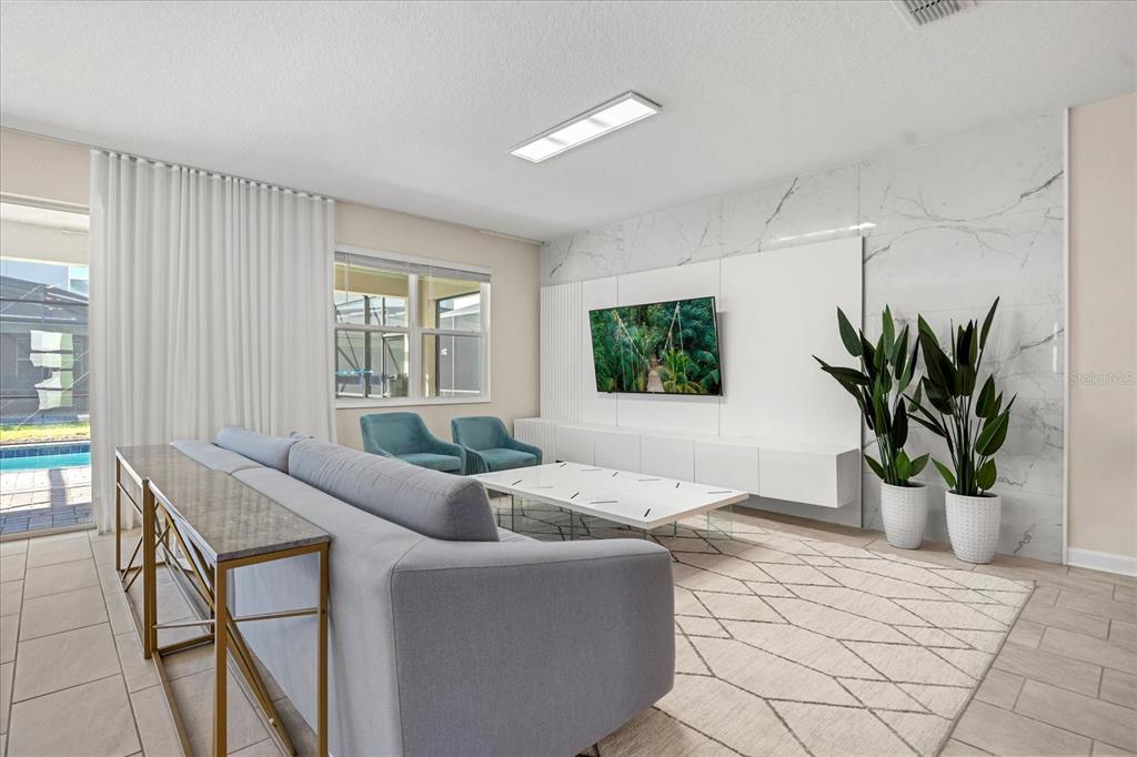 A modern living room features a marble accent wall, a gray sofa, and pool views — 4548 TARGET BOULEVARD, KISSIMMEE, FL
