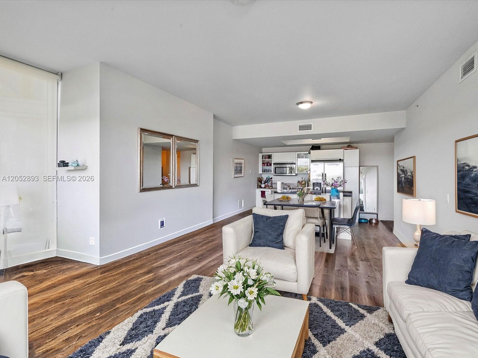 A living room with wood-look flooring, white furniture, and an open kitchen in the background — 888 Biscayne Blvd # 509, Miami FL 33132, MIAMI, FL