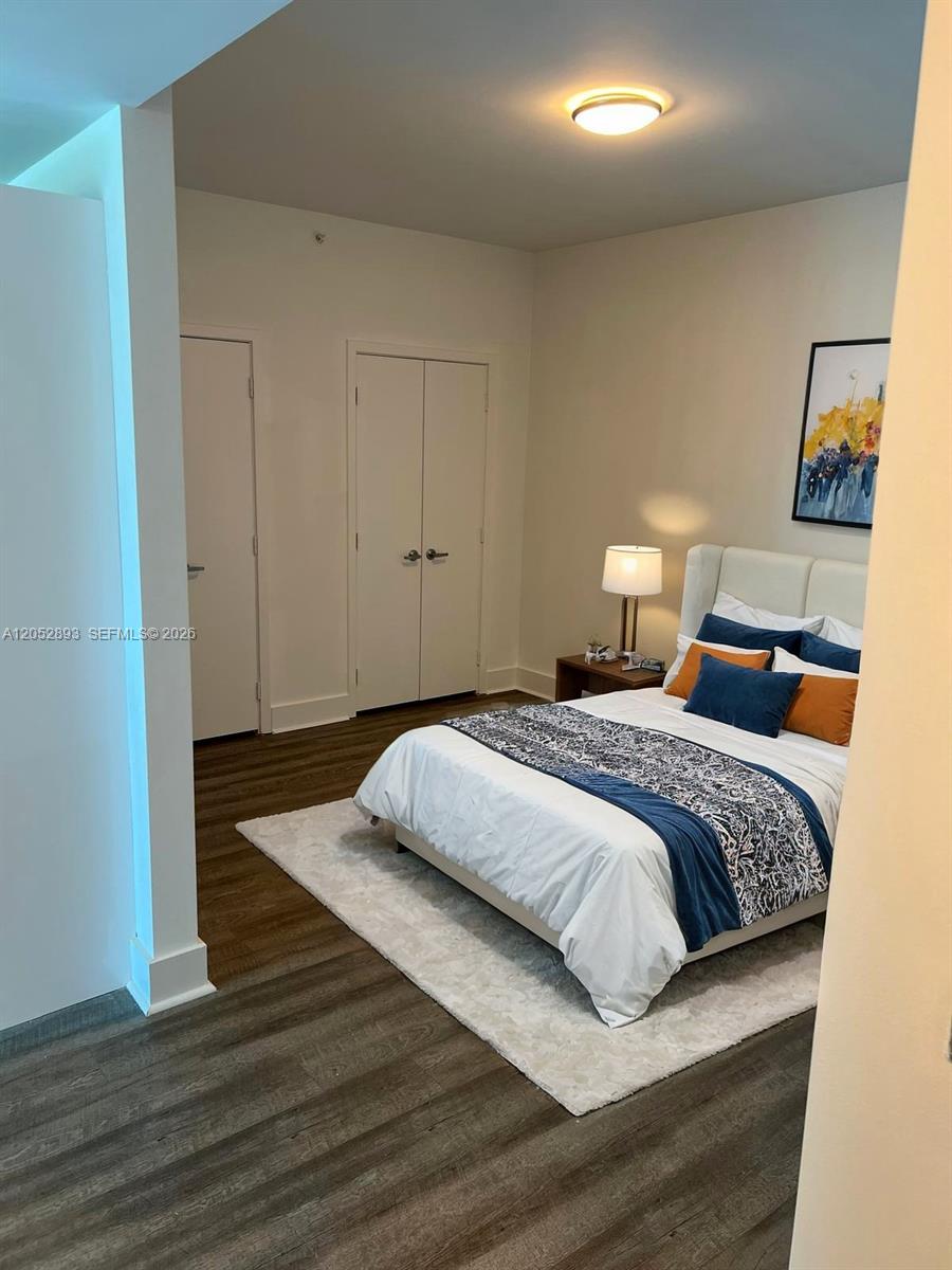 A bedroom features wood-look flooring, a white bed with blue and orange pillows, and closets — 888 Biscayne Blvd # 509, Miami FL 33132, MIAMI, FL