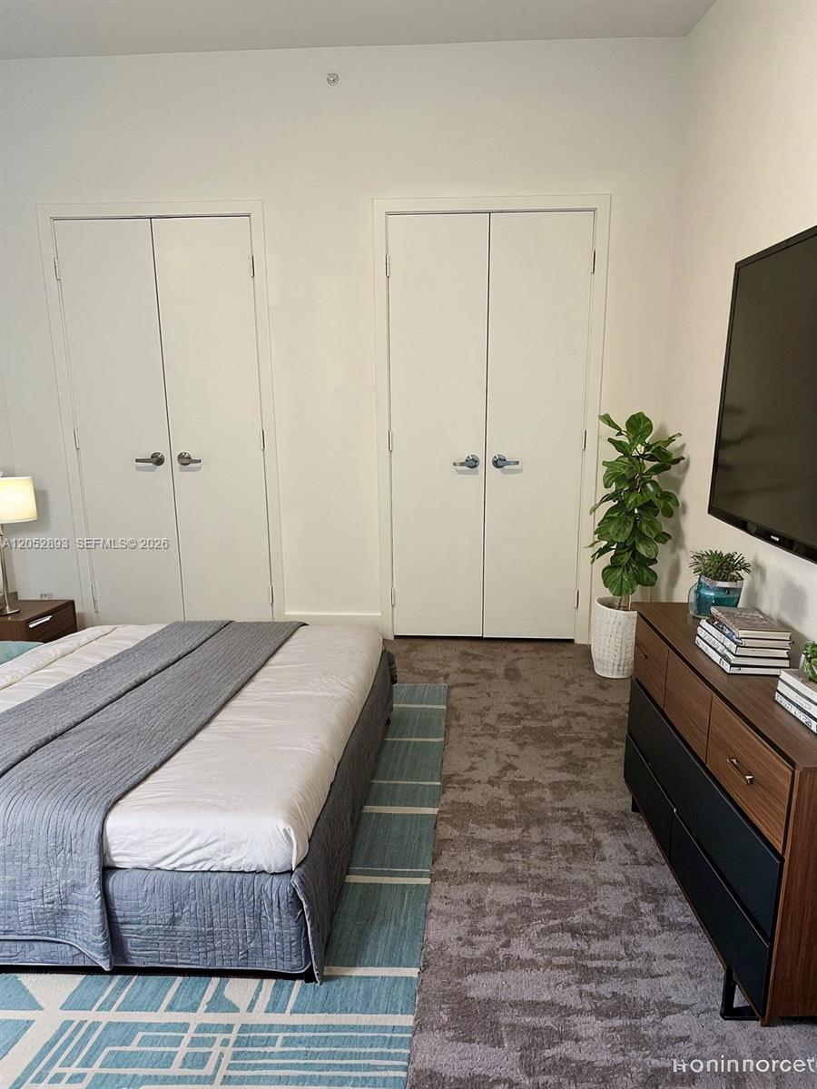 A bedroom features a bed, a dresser with a television, and two white closet doors — 888 Biscayne Blvd # 509, Miami FL 33132, MIAMI, FL