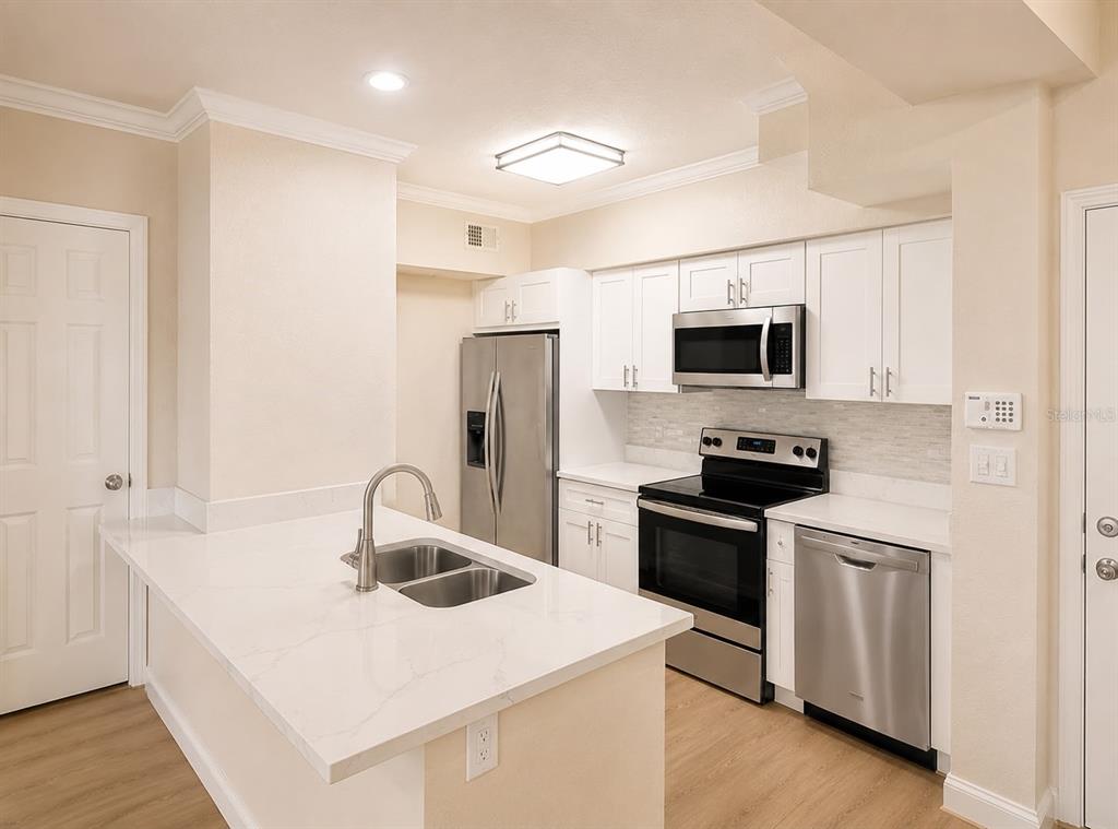 A kitchen with white cabinets, stainless steel appliances, and a quartz-topped island with a sink — 911 N ORANGE AVENUE UNIT 115, ORLANDO, FL