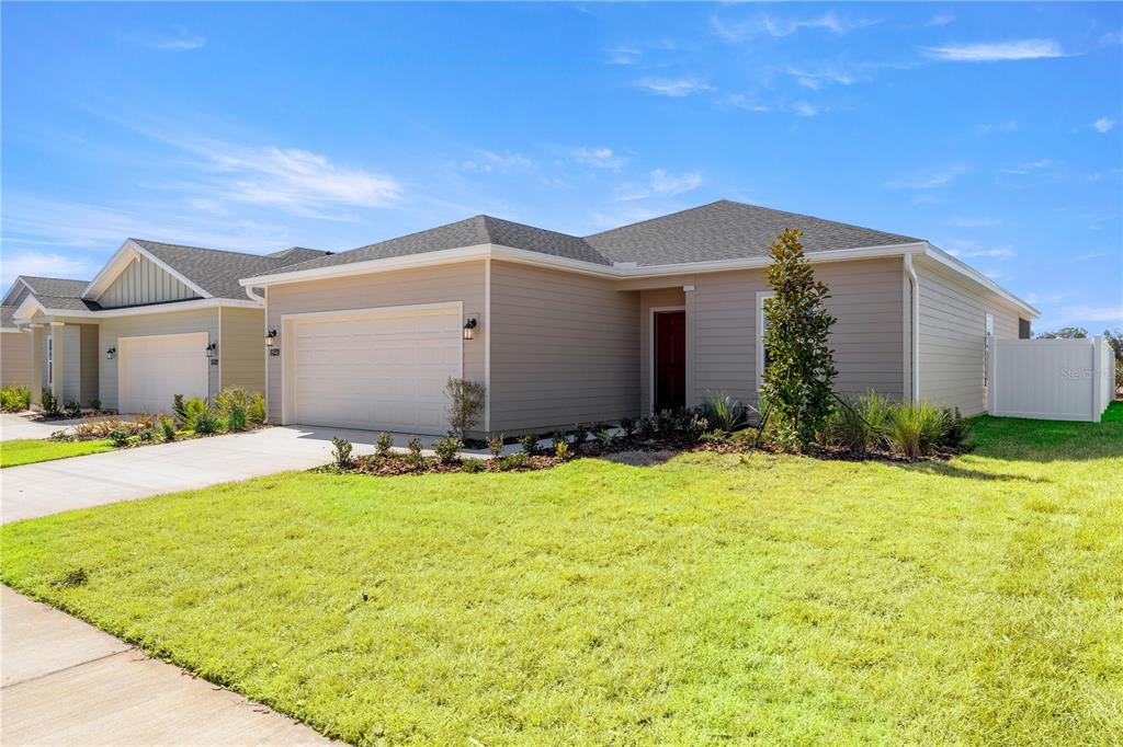 A beige single-story house with a two-car garage and a front lawn under a blue sky — 3578 NE 38TH LANE, OCALA, FL