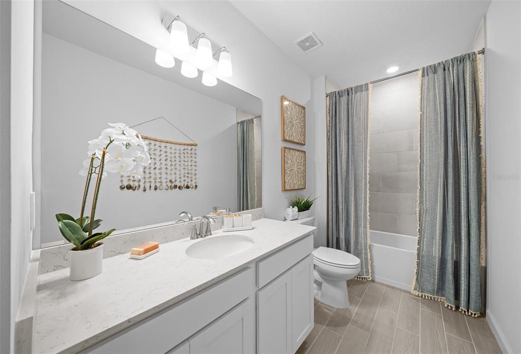 A bathroom features a white vanity with a quartz countertop, a mirror, and a tub-shower — 3578 NE 38TH LANE, OCALA, FL