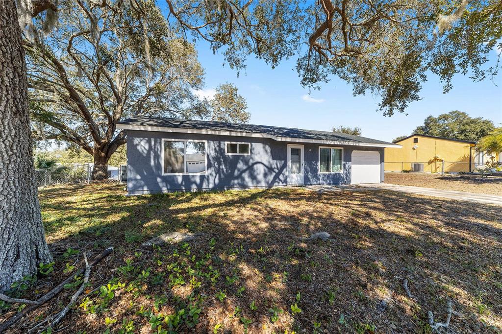 A single-story gray house with a white garage door sits under large oak trees — 6 HICKORY TRACK PASS, OCALA, FL