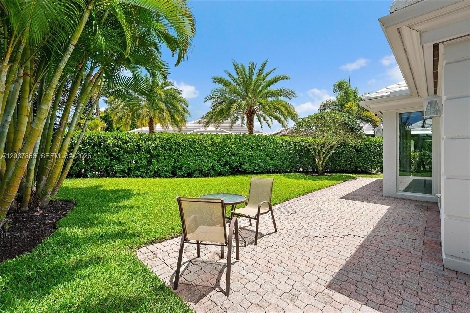 A patio with a small table and two chairs sits beside a grassy backyard — 4501 Captains Way, Jupiter FL 33477, JUPITER, FL