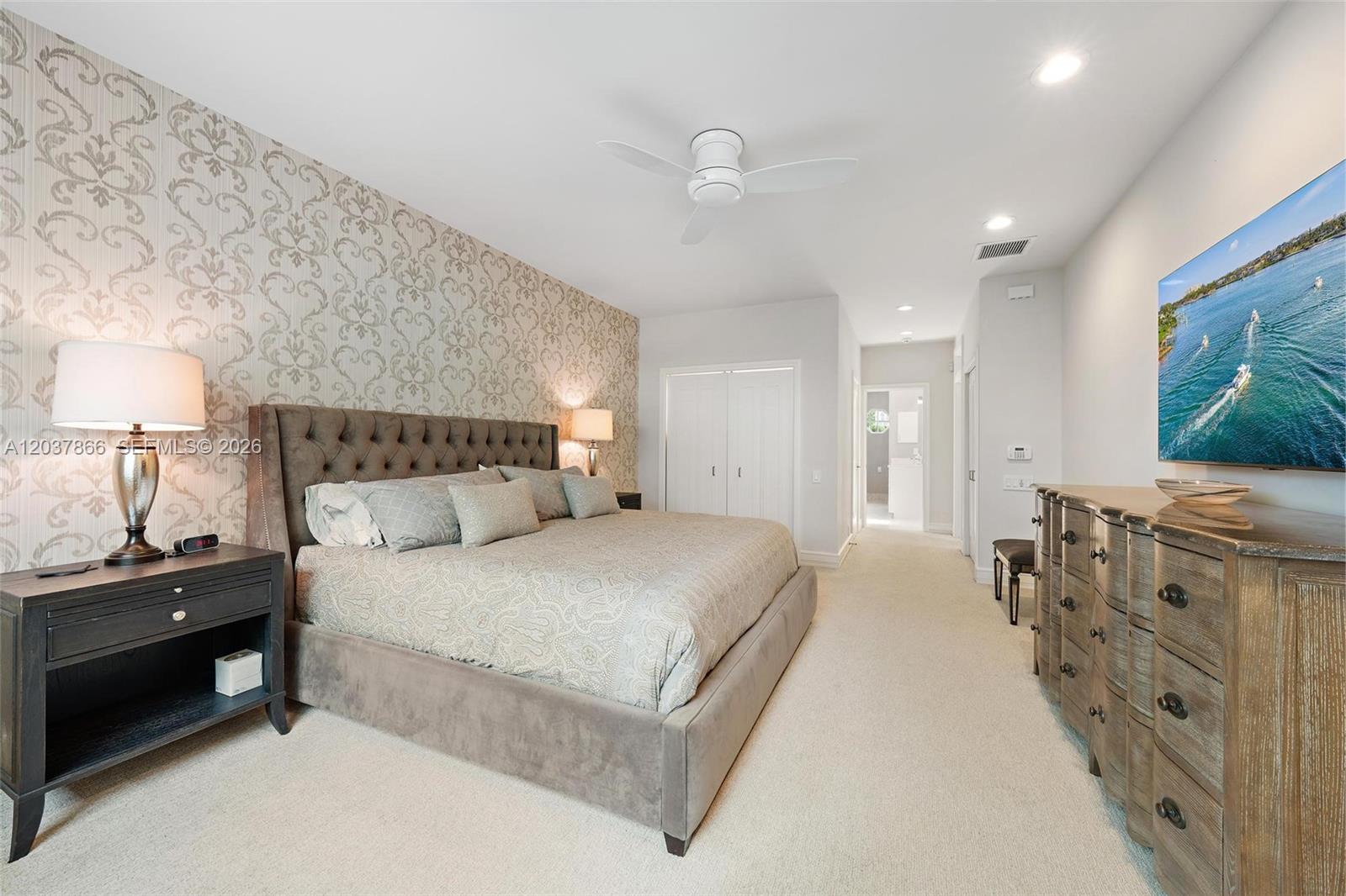 A bedroom features a tufted headboard, patterned wallpaper, a ceiling fan, and a wall-mounted television — 4501 Captains Way, Jupiter FL 33477, JUPITER, FL