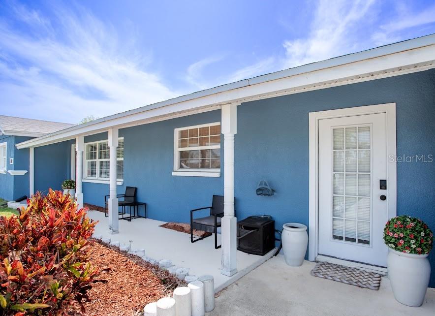 A blue house exterior features a covered porch with two chairs and potted plants — 225 RICHLAND, MERRITT ISLAND, FL