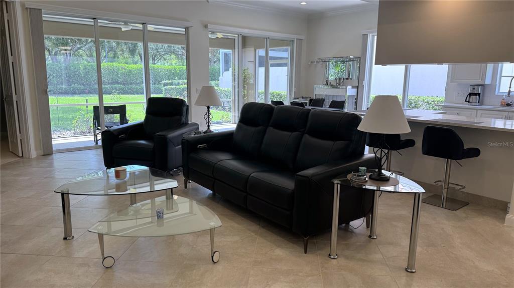 A living room with black leather furniture, glass tables, and large sliding glass doors — 4402 NOVATO COURT, NAPLES, FL