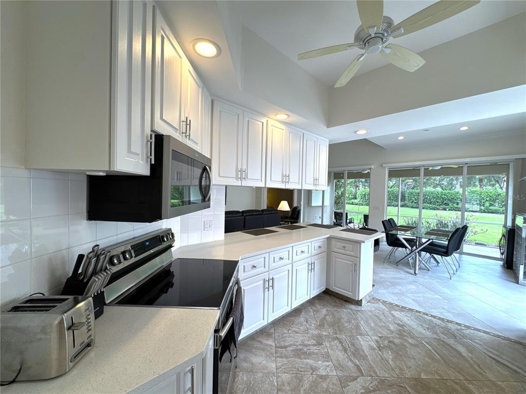 A kitchen with white cabinets, stainless steel appliances, and tile flooring overlooks a dining area — 4402 NOVATO COURT, NAPLES, FL