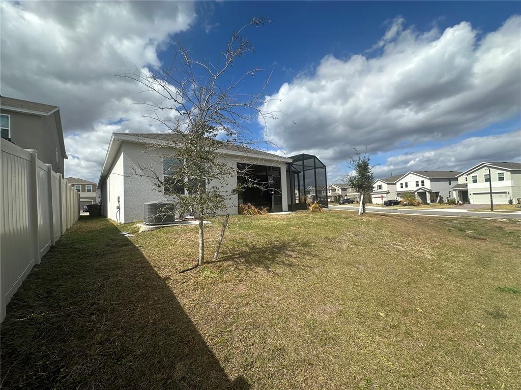 A view of a backyard with a white fence, a small tree, and a screened patio — 7776 MARSALA STREET, CLERMONT, FL