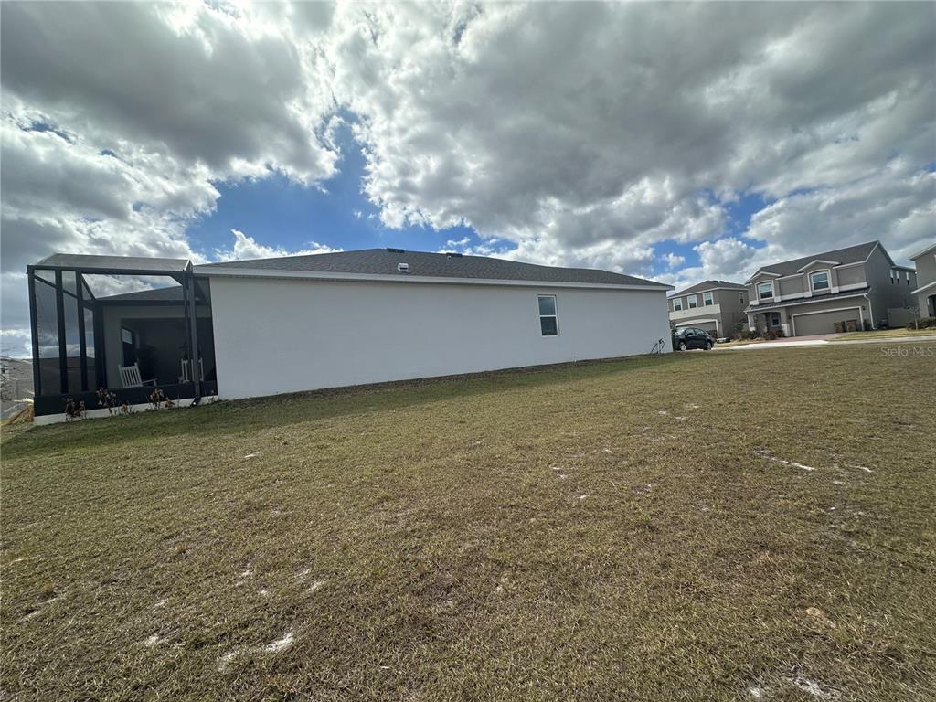 The exterior side view of a house features a screened-in patio and a large lawn — 7776 MARSALA STREET, CLERMONT, FL