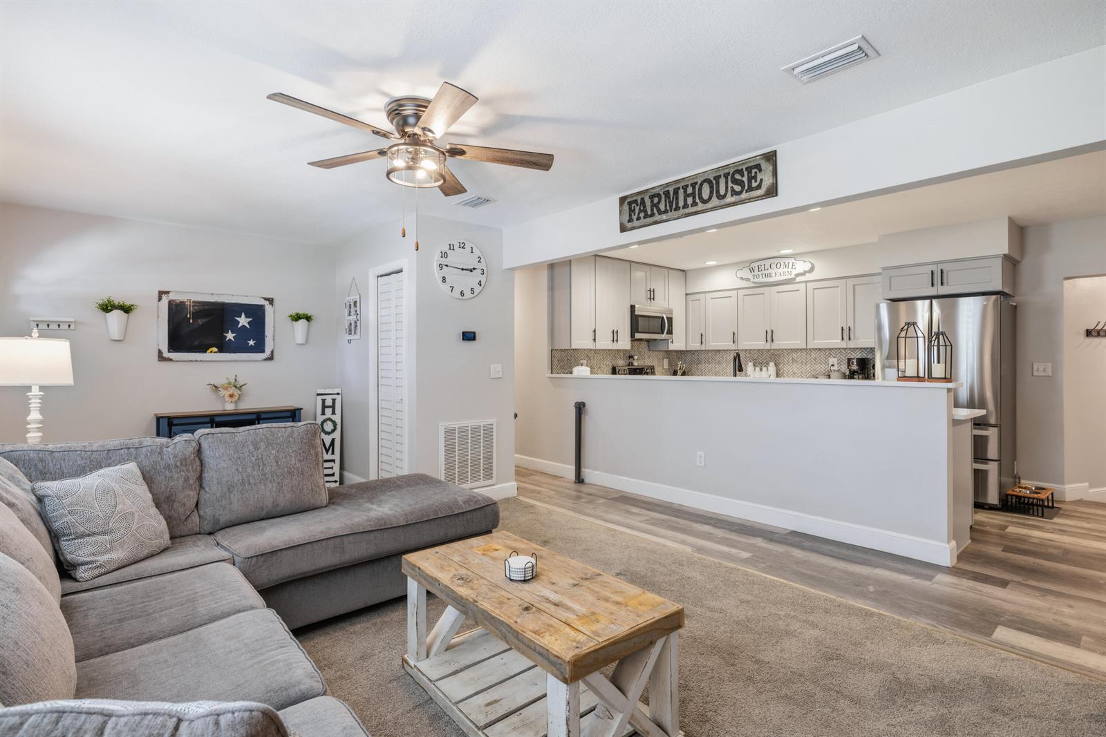 A living room with a grey sectional sofa opens to a kitchen with white cabinets — 305 17th Avenue, Vero Beach FL 32962, VERO BEACH, FL