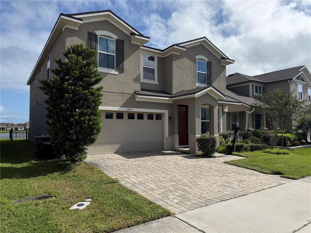 A two-story suburban house with a tan stucco exterior, a paved driveway, and a garage — 2489 BLOWING BREEZE AVENUE, KISSIMMEE, FL