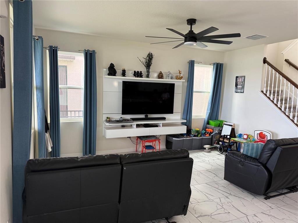 A living room features a wall-mounted entertainment center, black leather furniture, and tile flooring — 2489 BLOWING BREEZE AVENUE, KISSIMMEE, FL