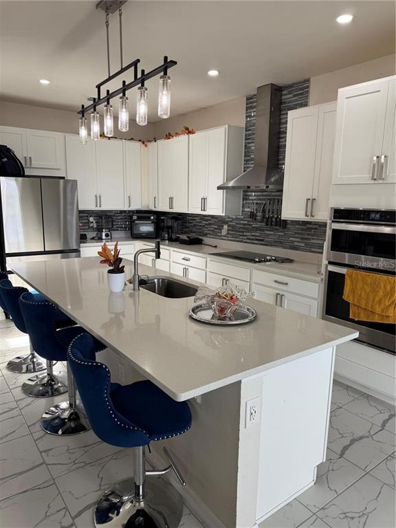 A modern kitchen features white cabinets, a large quartz island, and blue velvet bar stools — 2489 BLOWING BREEZE AVENUE, KISSIMMEE, FL
