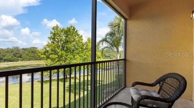 A screened-in balcony with a wicker chair overlooks a grassy lawn, trees, and a pond — 2847 OAKWATER DRIVE UNIT 2847, KISSIMMEE, FL