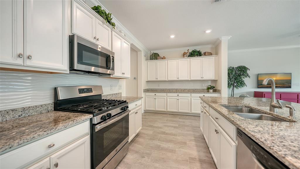 A kitchen features white cabinets, granite countertops, stainless steel appliances, and light-colored tile flooring — 17241 BLUE RIDGE PLACE, BRADENTON, FL