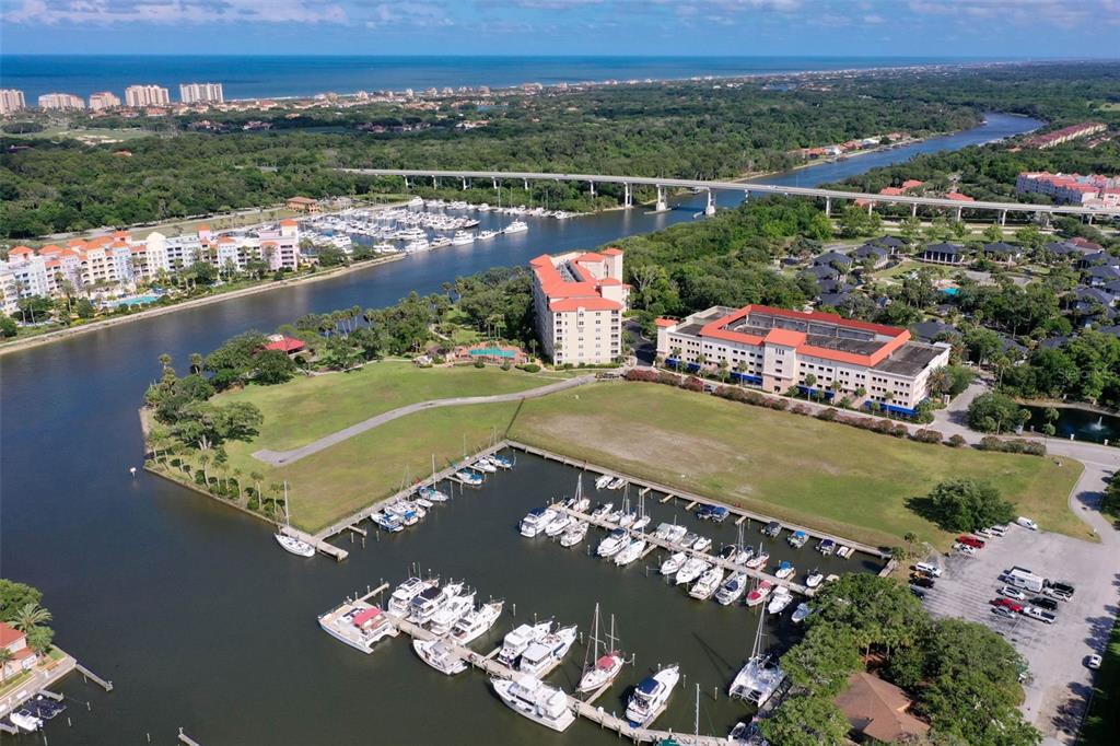 An aerial view shows a marina with docked boats, large residential buildings, and a bridge — 146 PALM COAST RESORT BOULEVARD UNIT 405, PALM COAST, FL