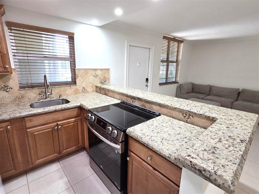 A kitchen with wood cabinets, granite countertops, and a black stove overlooks a living area — 2400 NE 10th St # 104, Pompano Beach FL 33062, POMPANO BEACH, FL