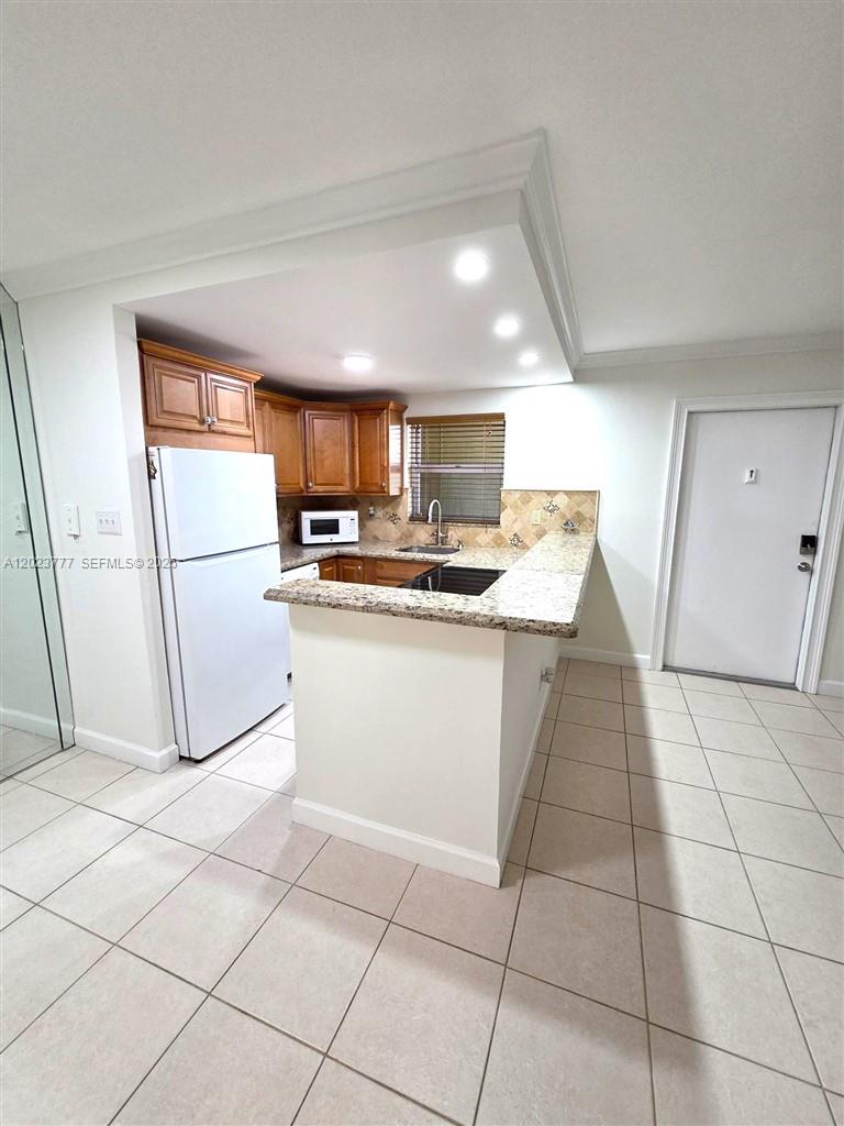 A kitchen features wood cabinets, granite countertops, a white refrigerator, and light-colored tile flooring — 2400 NE 10th St # 104, Pompano Beach FL 33062, POMPANO BEACH, FL