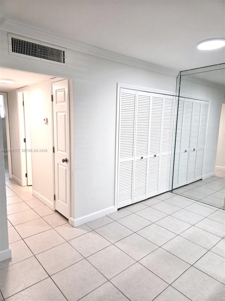 A hallway features white tiled floors, louvered closet doors, and a mirrored wall — 2400 NE 10th St # 104, Pompano Beach FL 33062, POMPANO BEACH, FL