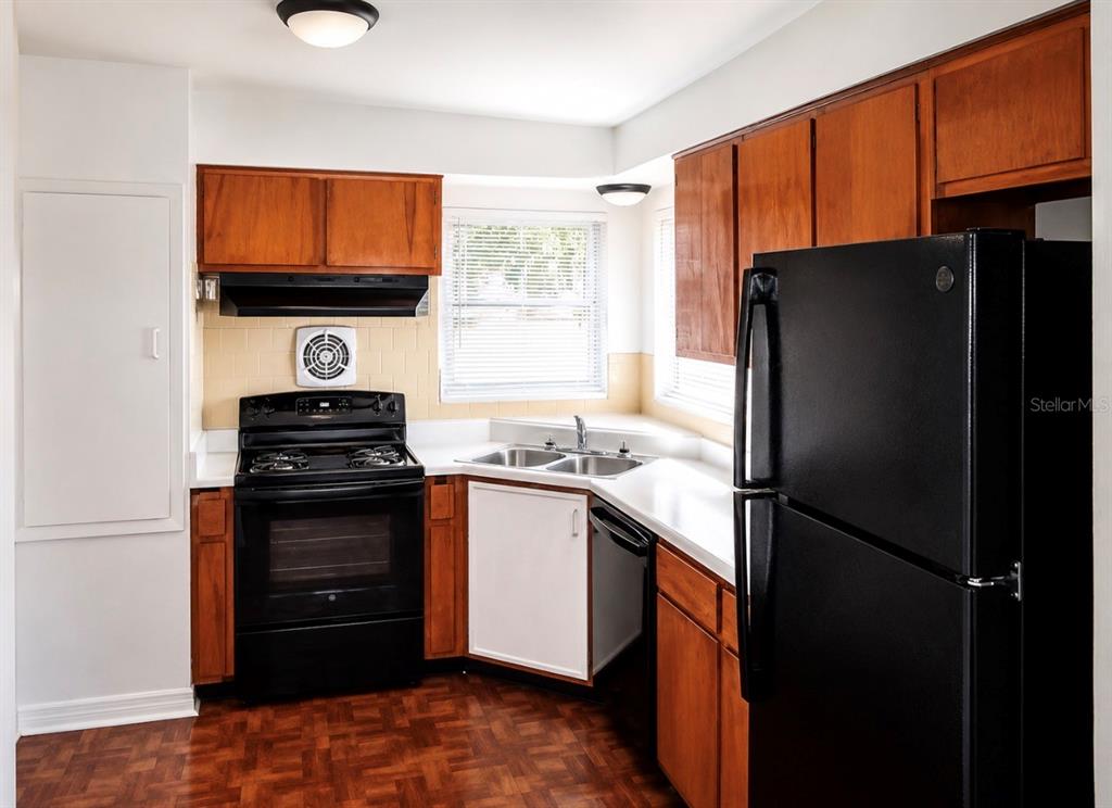 A kitchen features wood cabinets, black appliances, white countertops, and a parquet wood floor — 446 NEW YORK AVENUE, DUNEDIN, FL