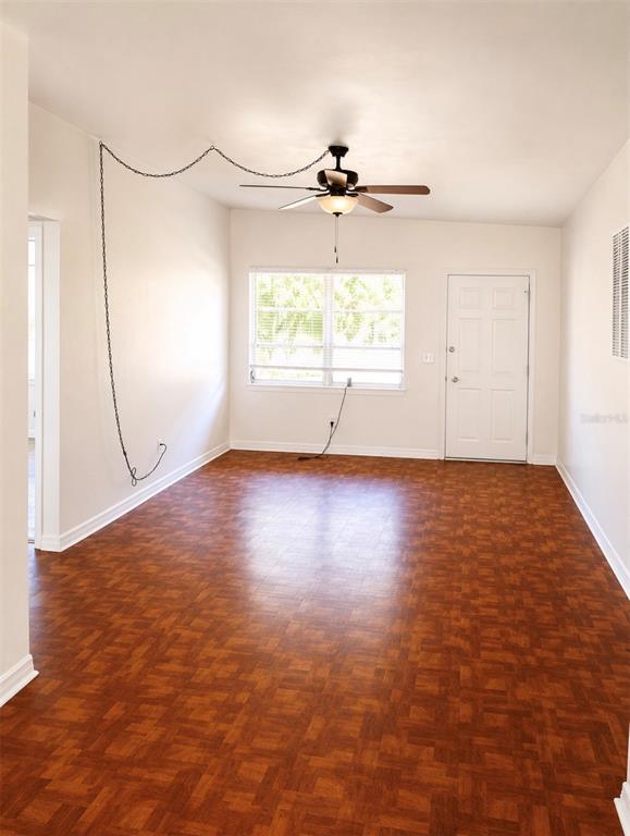 An empty room features wood-look flooring, a ceiling fan with a chain, and a white door — 446 NEW YORK AVENUE, DUNEDIN, FL