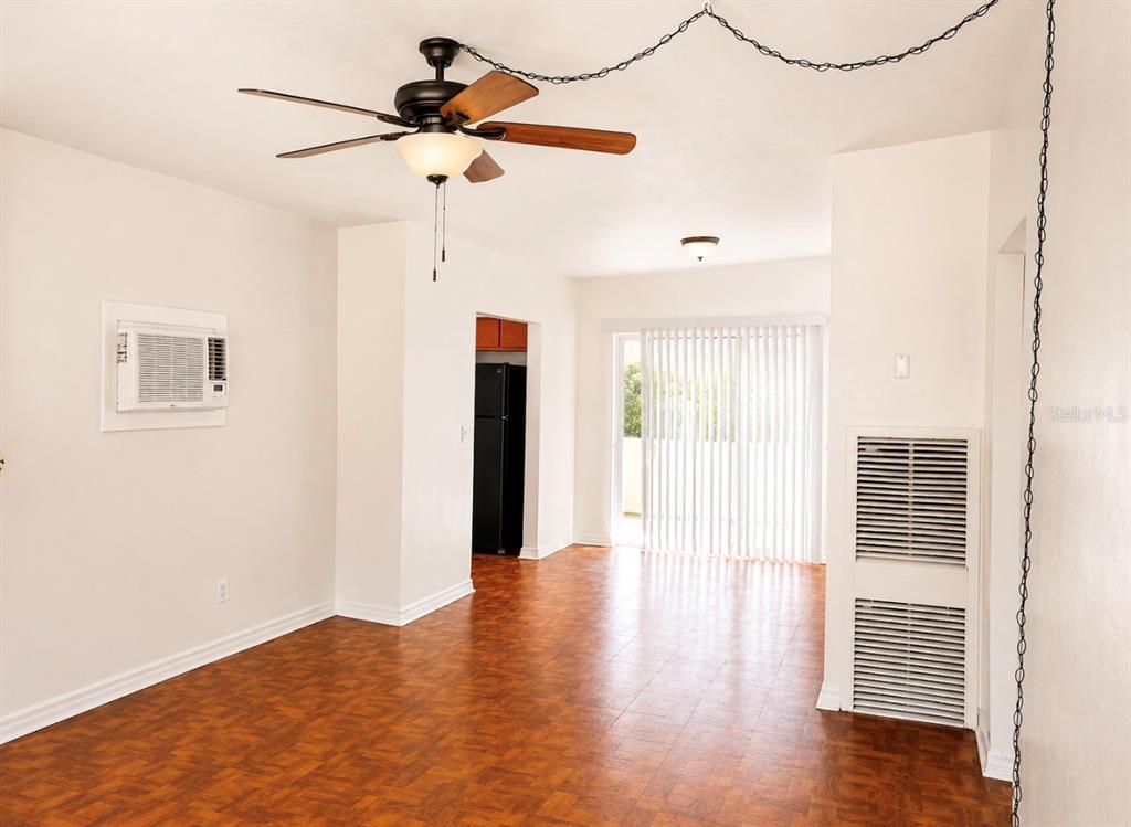 An empty room features wood-look flooring, a ceiling fan, a wall air conditioner, and blinds — 446 NEW YORK AVENUE, DUNEDIN, FL