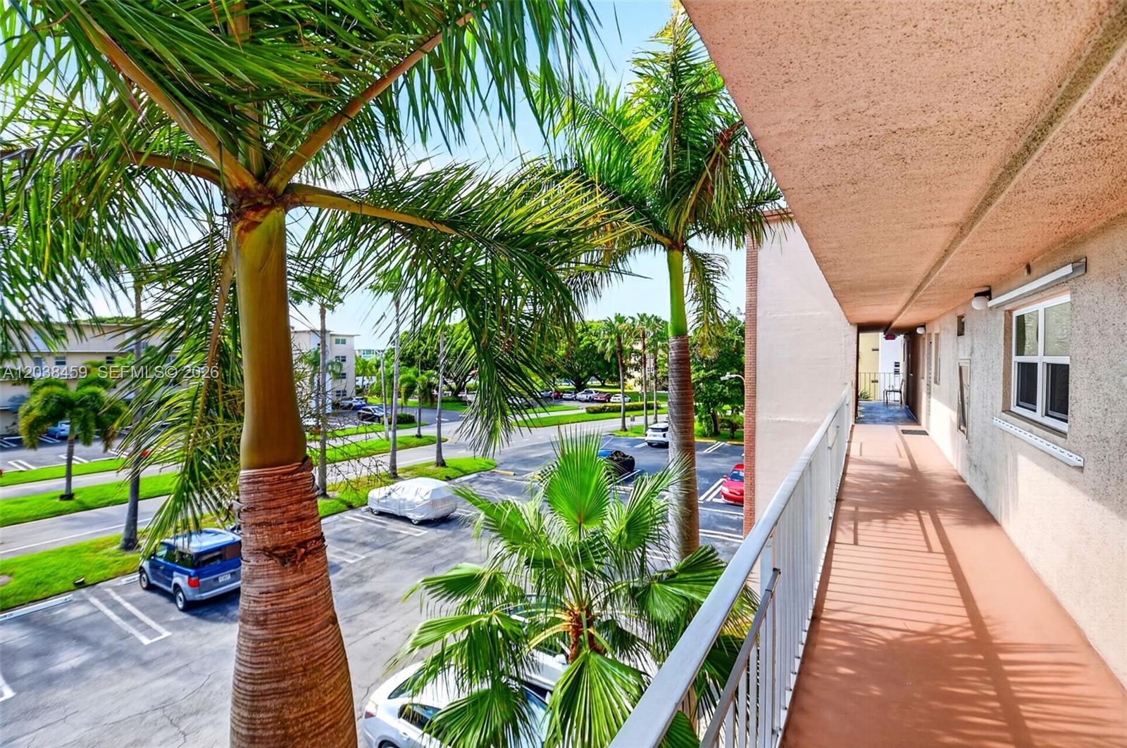 An outdoor balcony overlooks a parking lot with palm trees and several parked cars — 2615 NE 1st Ct # 303, Boynton Beach FL 33435, BOYNTON BEACH, FL