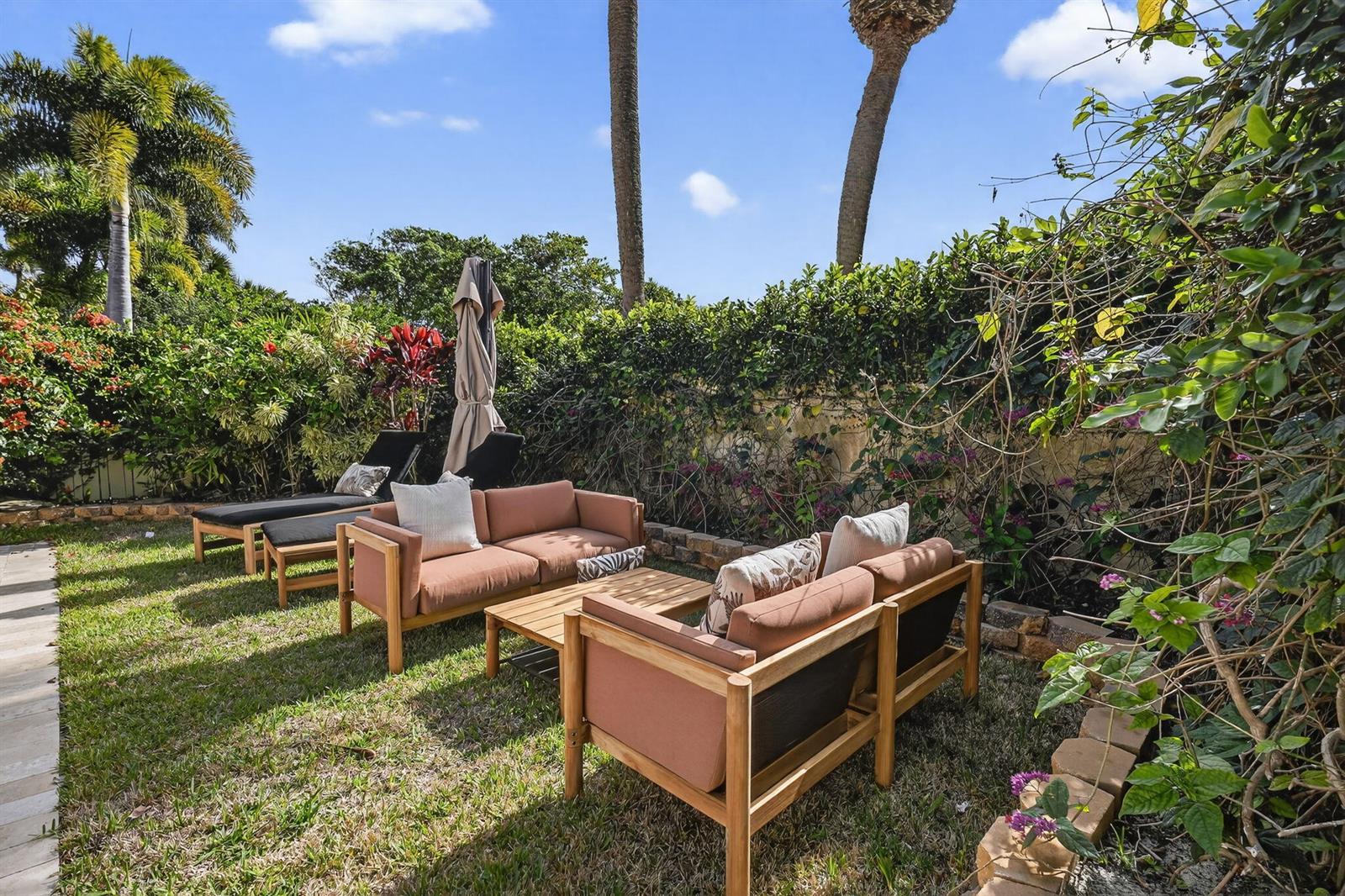 A backyard patio features outdoor furniture, lounge chairs, and lush landscaping under a blue sky — 3069 Mainsail Circle, Jupiter FL 33477, JUPITER, FL
