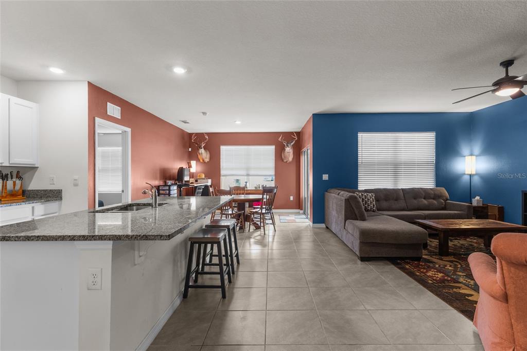 An open-concept kitchen and living area features tile flooring, granite countertops, and blue accent walls — 3637 DIVING DOVE LANE, BARTOW, FL