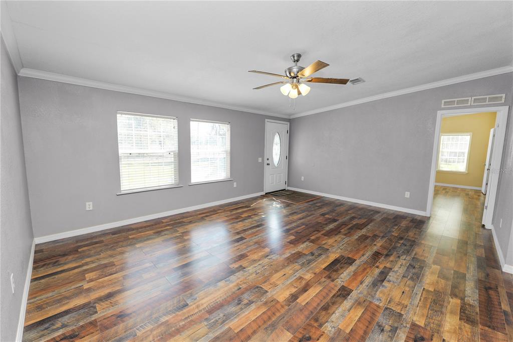 A living room with gray walls, wood-look flooring, a ceiling fan, and an entry door — 7405 SHOUPE ROAD, PLANT CITY, FL