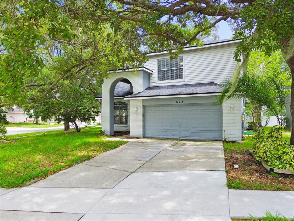 A two-story house with a white brick facade, a gray garage door, and a concrete driveway — 12914 LONGCREST DRIVE, RIVERVIEW, FL