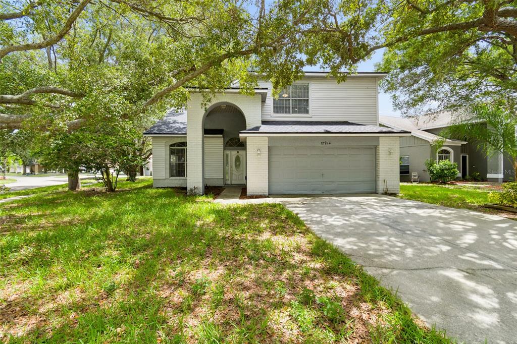 A two-story house with a white brick entryway, gray garage door, and large shade trees — 12914 LONGCREST DRIVE, RIVERVIEW, FL